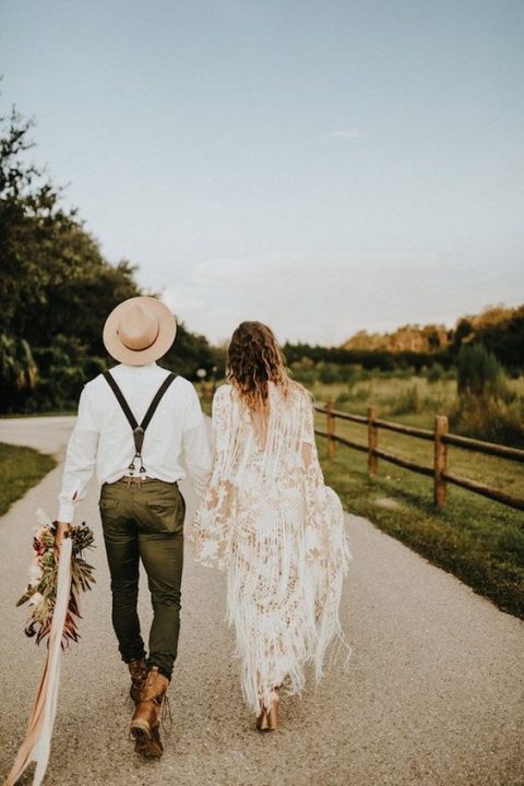 a boho groom's outfit with green pants, brown boots, a white shirt, suspenders and a neutral hat