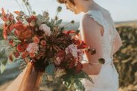a bold and lush fall wedding bouquet of pink, rust, deep red and deep purple blooms, greenery, seed pods and long ribbons is amazing