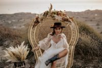 a bold boho bridal look with a semi sheer tulle wedding dress with a deep neckline, black embroidered cowgirl boots, a black flower embellished hat