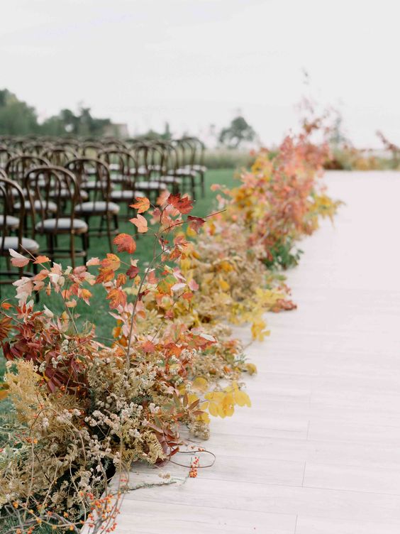 a bold fall wedding aisle with a runner and bright fall leaves and dried flowers is a cool idea for an autumn wedding