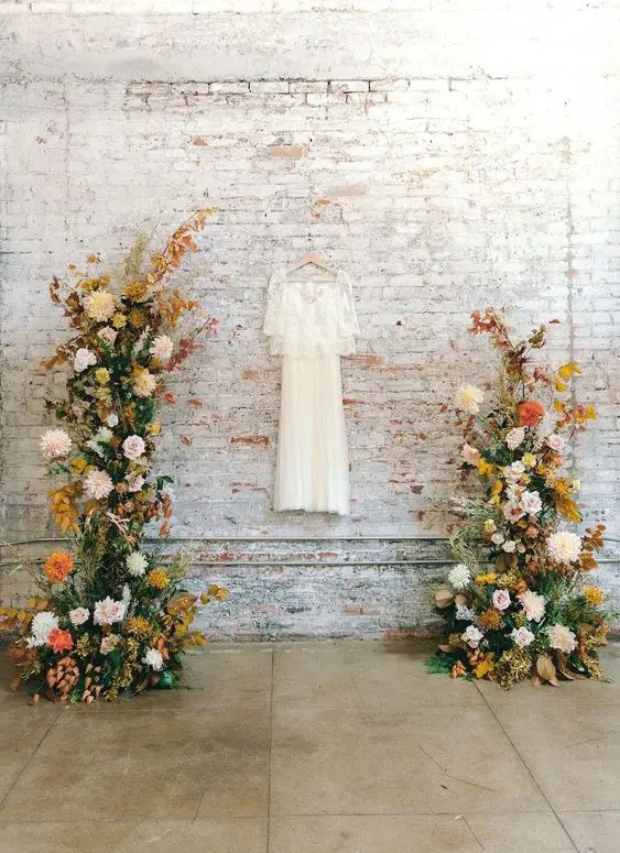 a bold fall wedding altar done with greenery, bright fall leaves, blush, white, mustard and orange dahlias is amazing