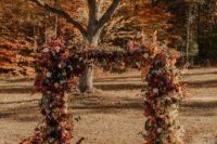 a bold fall wedding arch decorated with neutral and bright foliage, bold blooms and thistles is a cool idea for a fall wedding