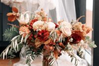 a bold fall wedding bouquet of white, blush and burgundy blooms, greenery and fall foliage is chic