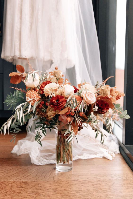 a bold fall wedding bouquet of white, blush and burgundy blooms, greenery and fall foliage is chic