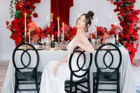 a bold rounded arch covered with red roses and matching red roses on the table for a refined and chic wedding tablescape