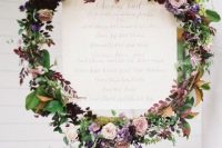 a bright and cool fall wedding wreath of blush, deep purple, lilac and white blooms, greenery and dark foliage and a wedding toast inside