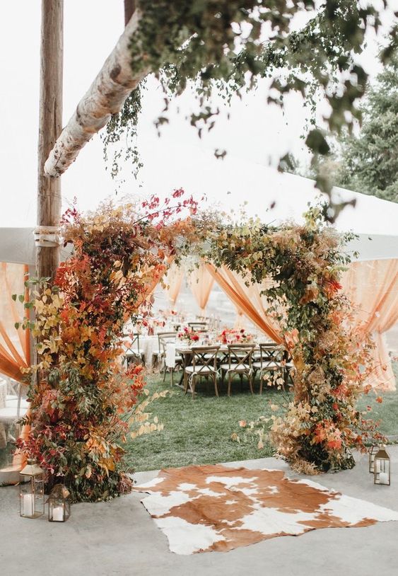 a bright fall wedding arch covered with greenery and bold foliage is a stunning idea for a fall wedding