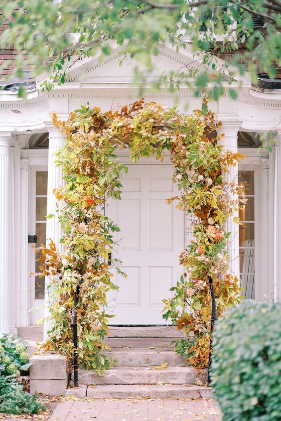 a bright fall wedding arch covered with greenery, bold foliage and blush blooms is a stunning idea for a fall wedding