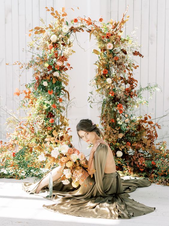 a bright fall wedding arch covered with greenery, bold leaves and blush and rust blooms looks amazing