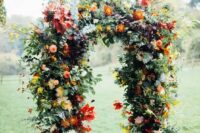 a bright fall wedding arch with red and yellow blooms, greenery, berries and fall leaves for a statement