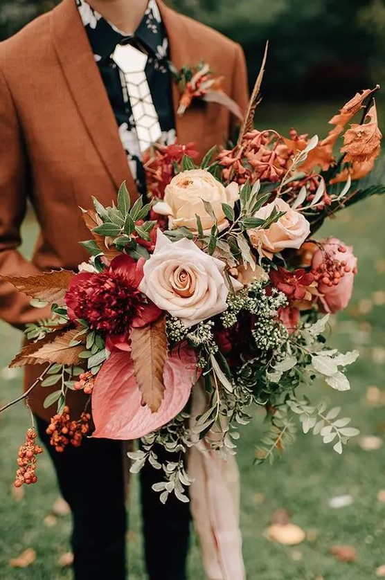 a bright fall wedding bouquet of blush, neutral, deep red and pink blooms, greenery, berries and twigs with long ribbons is amazing