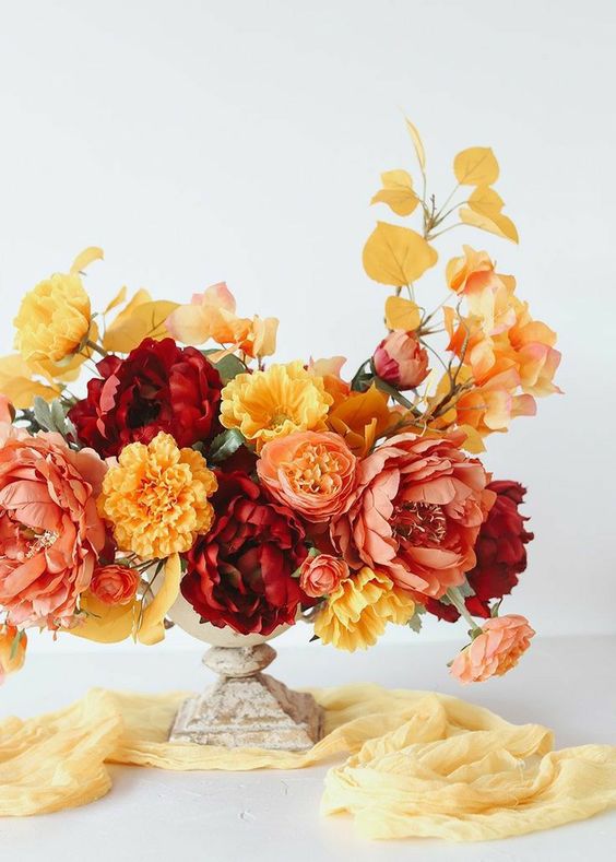 a bright fall wedding centerpiece of yellow, blush and burgundy blooms, bold leaves in a vintage urn is a chic and bright idea