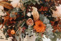 a bright fall wedding centerpiece with a white vintage urn, greenery, lots of blooms in orange, blush, rust and coffee shades