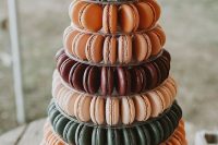 a bright macaron wedding tower with grene, orange and burgundy ones, with white and orange blooms on top, with greenery