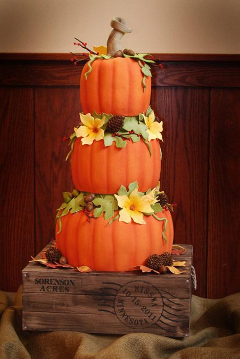 a bright pumpkin tiered wedding cake with faux leaves, blooms and pinecones, with twigs and berries is all fall-inspired