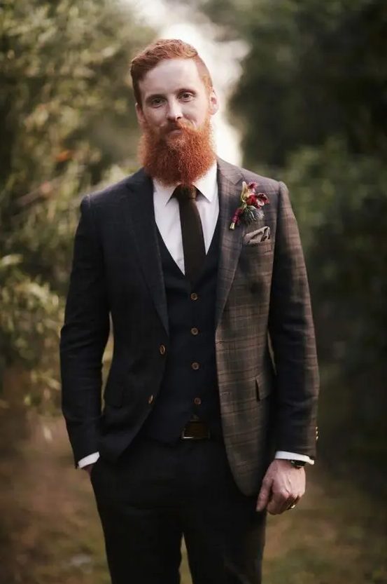 a brown plaid three-piece suite with a brown tie and a white shirt, a taupe handkerchief and a bold floral boutonniere