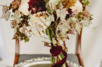 a catchy fall wedding bouquet of white and burgundy blooms, fall foliage and burgundy velvet ribbon is adorable