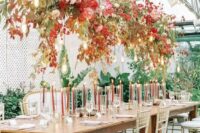a chic fall wedding reception space with a lovely overhead floral installation with neutral and bright blooms and leaves plus bulbs over the table