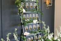 a chic ladder drink stand with greenery and white florals is a cool idea for many weddings