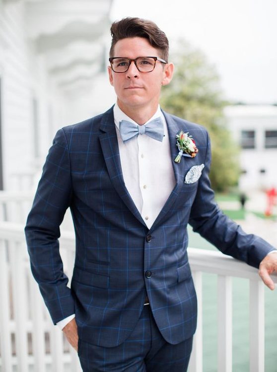 a chic navy windowpane print suit, a white shirt, a powder blue bow tie and a colorful floral boutonniere