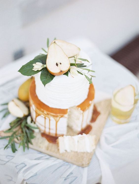 a chic white wedding cake with caramel, foliage and white blooms and cut pears is a fantastic idea for a fall wedding