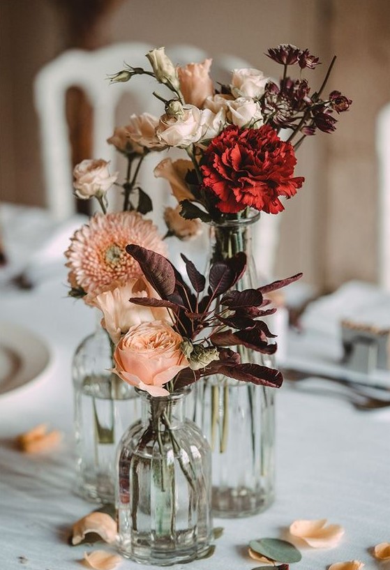 a cluster wedding centerpiece of vases with dark foliage, blush and red blooms is very lovely for fall