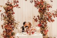a colorful fall wedding arch with bold leaves and pink and blush blooms is an adorable solution for a bold fall wedding