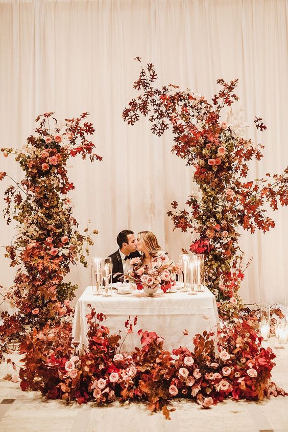 a colorful fall wedding arch with bold leaves and pink and blush blooms is an adorable solution for a bold fall wedding