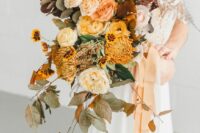 a colorful fall wedding bouquet of blush and peachy blooms, mustard ones, greenery and dark foliage is gorgeous