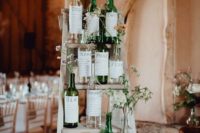 a creative wedding chart of wine bottles with stickers and greenery and wildflowers for a vineyard wedding
