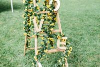 a cute rustic wedding decoration of a ladder, greenery, sunflowers and wooden letters is a cool idea