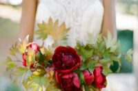 a deep red wedding bouquet withh fall leaf accents and a navy ribbon looks bright and cool