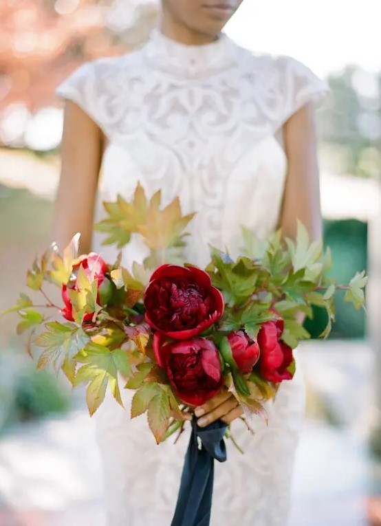 a deep red wedding bouquet withh fall leaf accents and a navy ribbon looks bright and cool