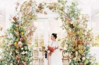 a fabulous and textural fall wedding arch with burgundy, pink and yellow blooms, greenery and fall foliage is amazing for an autumn celebration
