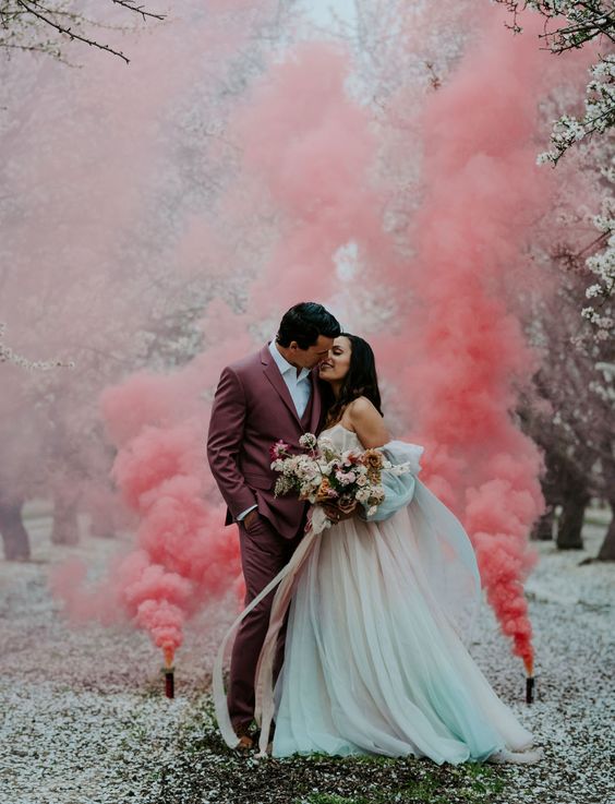 a fairy tale wedding portrait with pink smoke bombs, a groom in a mauve suit and a bride wearing an ombre off the shoulder wedding dress