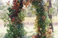 a fall wedding arch completely covered with green and bold fall leaves is a lovely idea for a fall wedding, it looks lovely and all-natural