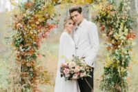 a fall wedding arch covered with greenery and bold fall foliage is a stunning idea for a fall wedding