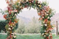 a fall wedding arch decorated with greenery, blush blooms, bold fall leaves and mustard flowers is a cool idea for the fall