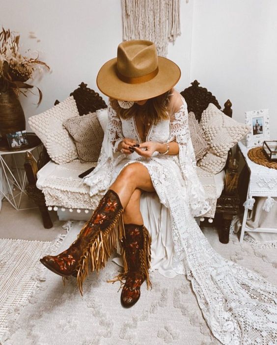 a fantastic boho bridal look with tall floral pattern and gold fringe cowboy boots, a boho lace A-line wedding dress with bell sleeves and a tan hat