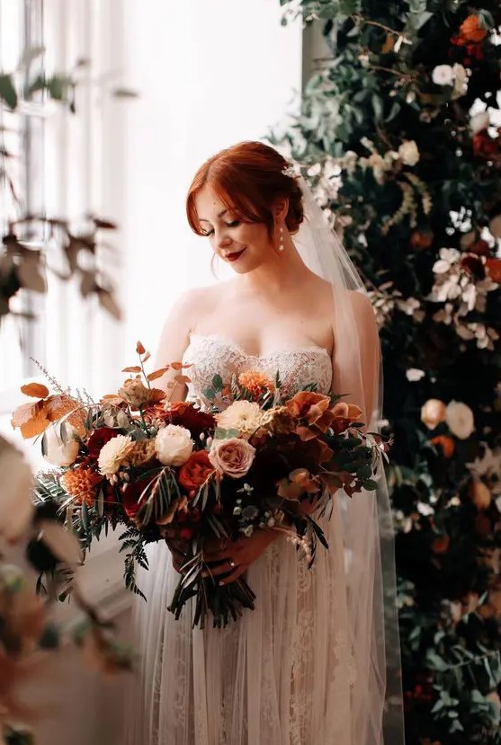 a fantastic lush and dimensional wedding bouquet of pink, blush, burgundy, rust blooms, greenery and berries plus bold fall leaves is gorgeous