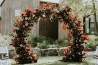 a fantastic round fall wedding arch with blush, burgundy and red blooms, greenery and colorful fall leaves and foliage is amazing