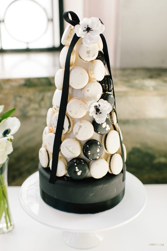 a fantastic wedding dessert with a black and white cake covered with black and white splatter macarons and a white bloom on top