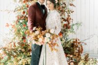 a gorgeous fall wedding arch decorated with greenery, bold fall foliage, rust and orange blooms looks wow