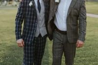a groom and groomsman wearing plaid and windowpane print suits, white shirts and white floral boutonnieres look cool