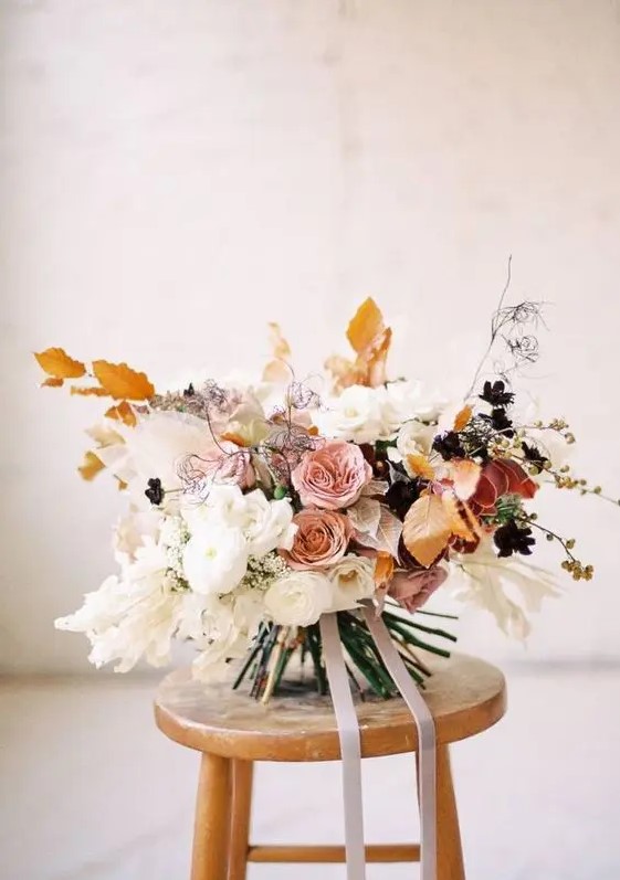 a jaw-dropping delicate-colored fall wedding bouquet of white, pink, rust blooms and fall-colored leaves and ribbons is very chic