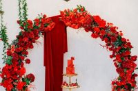 a jaw-dropping round red rose wedding arch with burgundy fabric, a gorgeous red wedding cake and lots of desserts