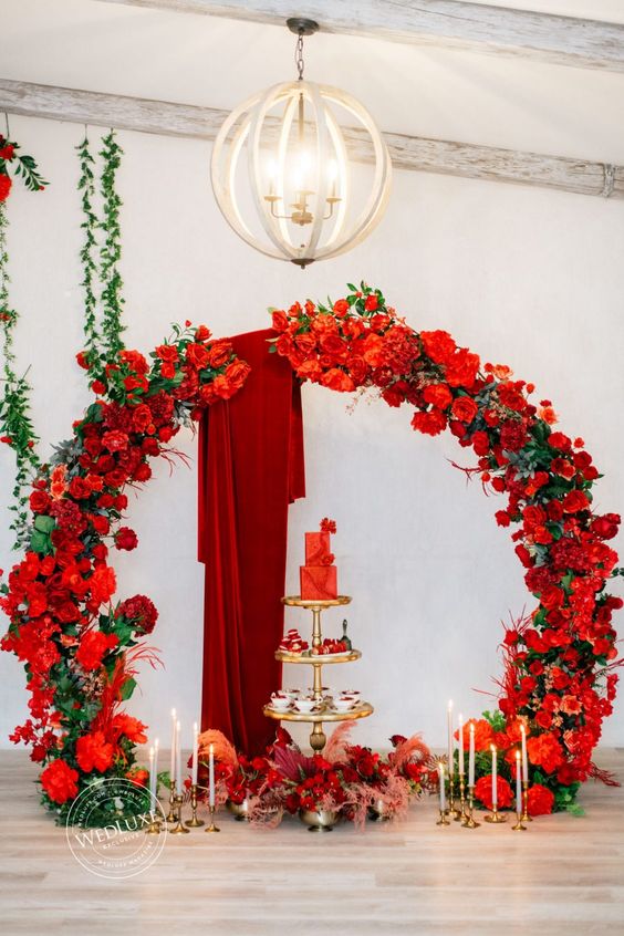 a jaw dropping round red rose wedding arch with burgundy fabric, a gorgeous red wedding cake and lots of desserts