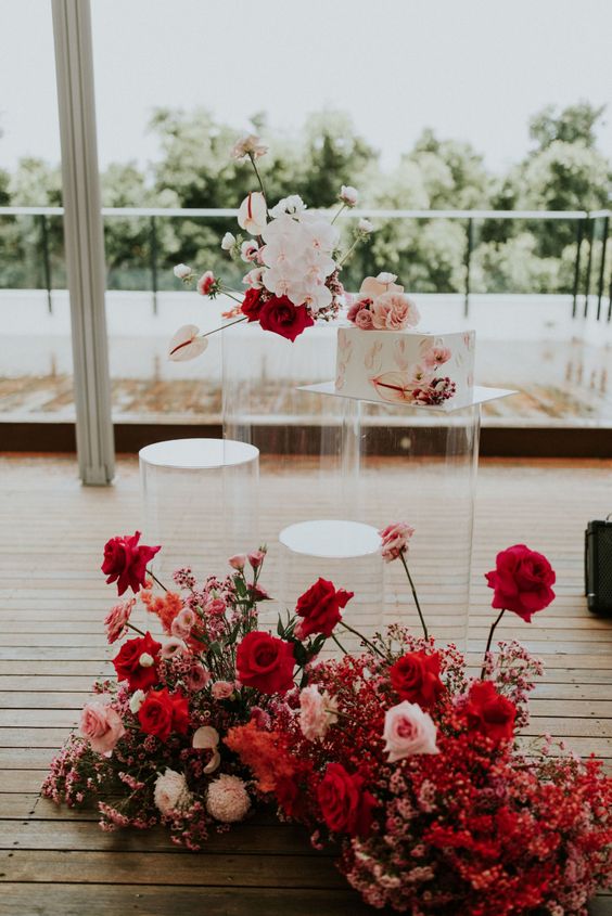 a jaw dropping wedding cake stand with super lush red and blush blooms, a clear wedding cake stand and some more blooms