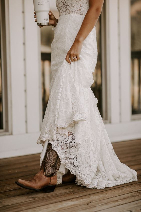 a lace A-line wedding dress with a train and brown patterned cowboy boots for a rustic and very chic bridal look at a fall wedding