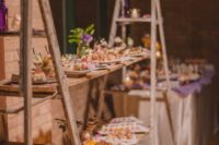 a large dessert station of two ladders and wooden planks, with greenery and blooms and lots of sweets